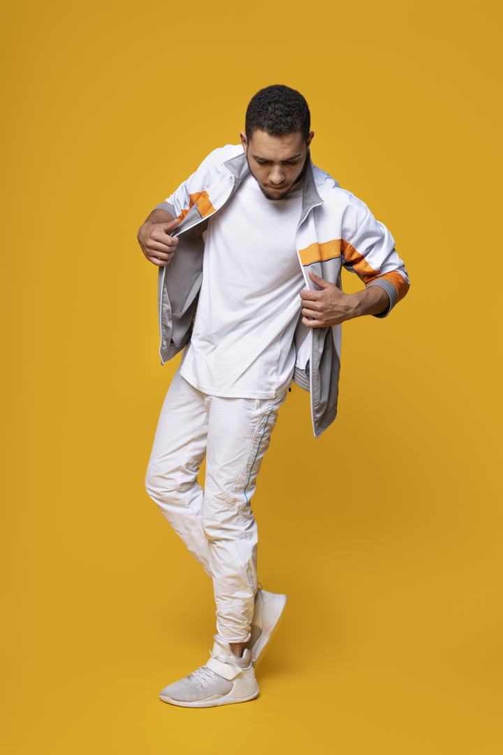 Male model in a white and orange tracksuit on a yellow set