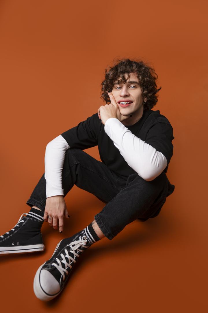 Curly-haired male model smiling on an orange backdrop