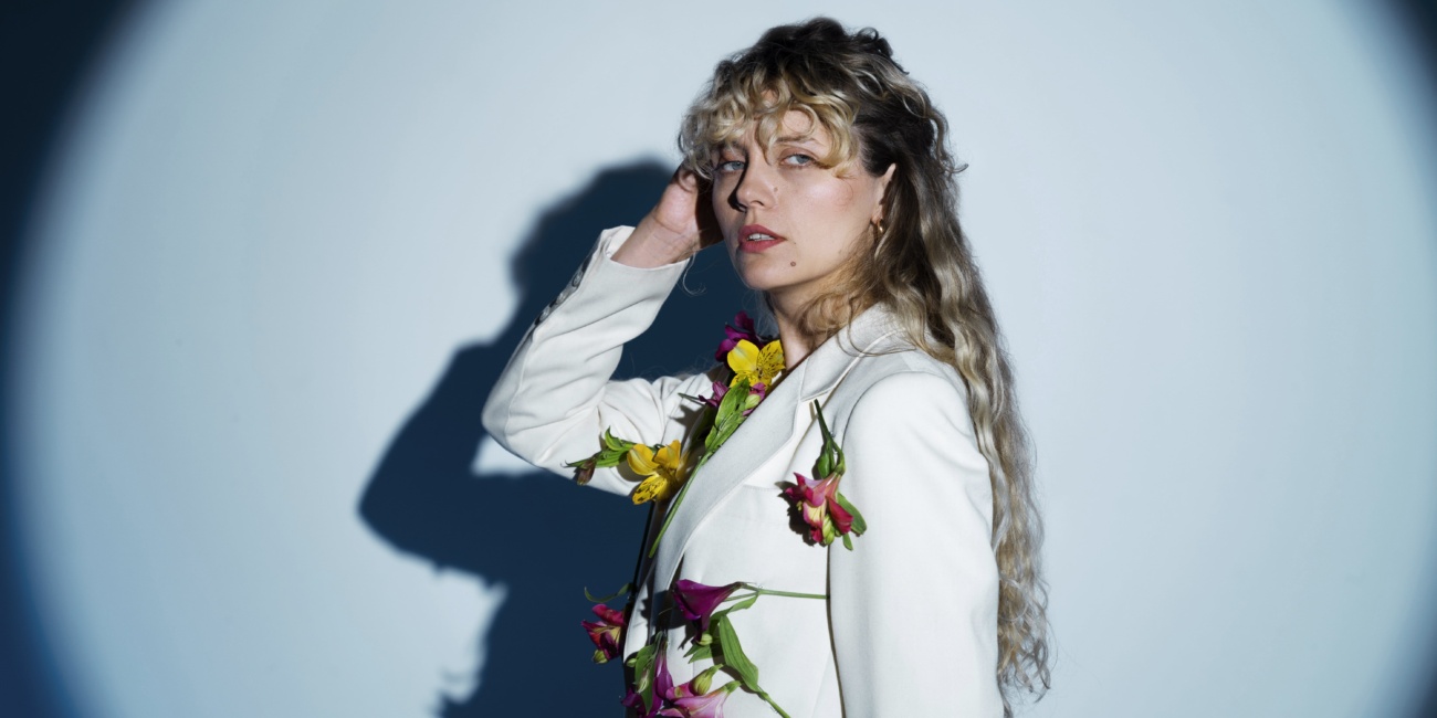 Model posing in a creative studio photo shoot wearing a white blazer decorated with flowers, under dramatic spotlight lighting.